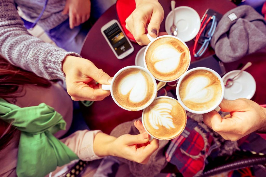 Imagen en la que se ven a un grupo de 4 amigos juntando sus tazas de café latte art mostrando sus dibujos y brindando.