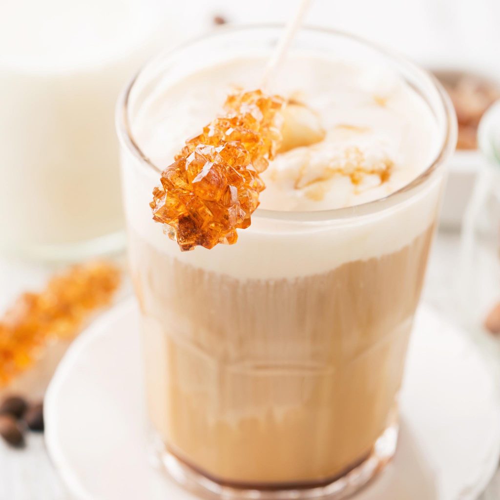 Latte Art que se aprecia en un vaso de excelente café con leche con una gruesa capa de sedosa crema adornado con virutas de miel caramelizada.